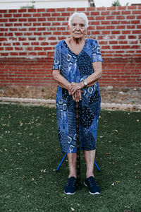 Portrait of smiling senior woman standing against brick wall