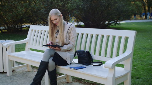 Woman using digital tablet while sitting on bench in park