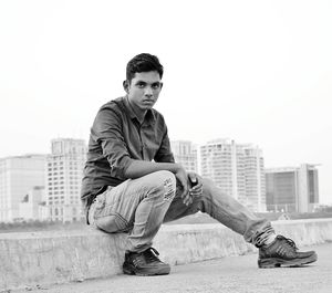 Portrait of young man sitting on curb against clear sky