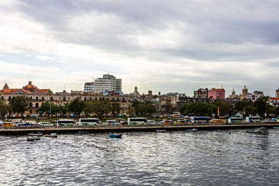 View of buildings by river against cloudy sky