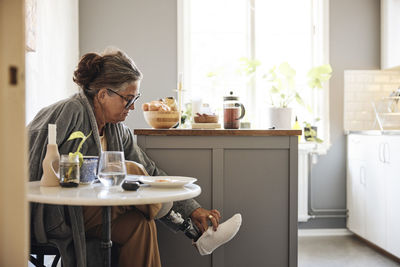 Mature woman wearing prosthetic leg while sitting at home