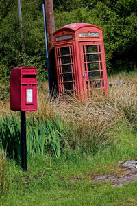 Red telephone booth on grass against plants