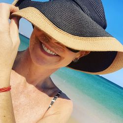 Close-up of smiling woman wearing hat at beach against sky