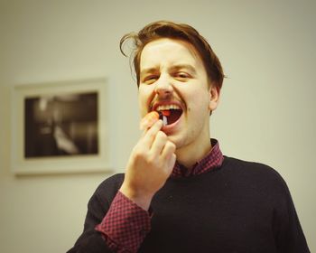 Portrait of man eating plastic sushi against wall at home