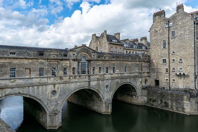 Arch bridge over river amidst buildings against sky