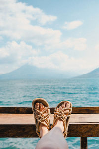 Low section of woman on pier over sea against cloudy sky