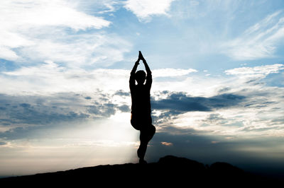 Silhouette person doing yoga against cloudy sky at dusk