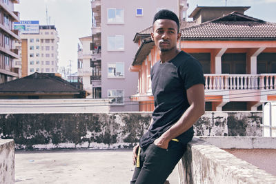 Young man looking away while standing against building 