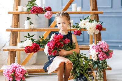 Portrait of girl sitting with flowers on wooden steps at home