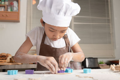 The little asian girl wore a white chef hat and a brown apron. the kid making cookies