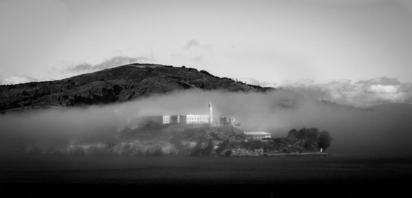 Alcatraz island in sea against mountain in foggy weather