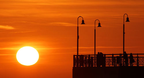 Silhouette street light by sea against orange sky in tuscany