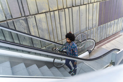 Stylish man carrying bicycle on escalator