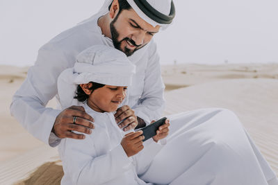 Father and son looking at smart phone while sitting at desert