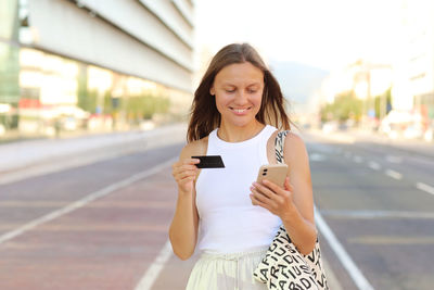 Beautiful smiling young woman consumer with credit card and smartphone looks in camera. people 