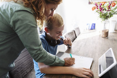 Mother helping smiling son in studying at home