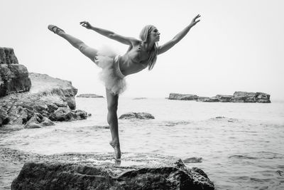 Full length of young woman dancing rock by sea against clear sky