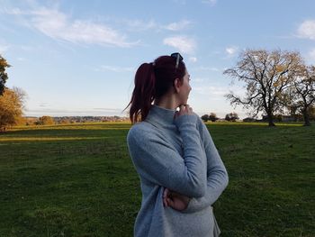 Side view of young woman standing on field against sky
