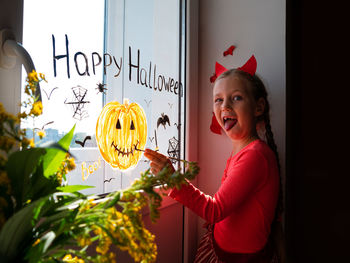 Child painting pumpkin window preparing celebrate halloween kid draws decorates room with paper bats