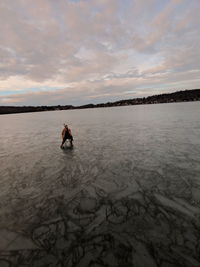 Mid adult woman sitting on frozen lake against cloudy sky during sunset