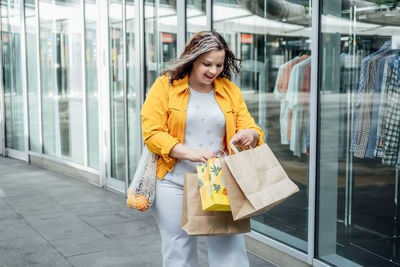 Happy confident smiling plus size curvy young woman with shopping bags walking on city street near