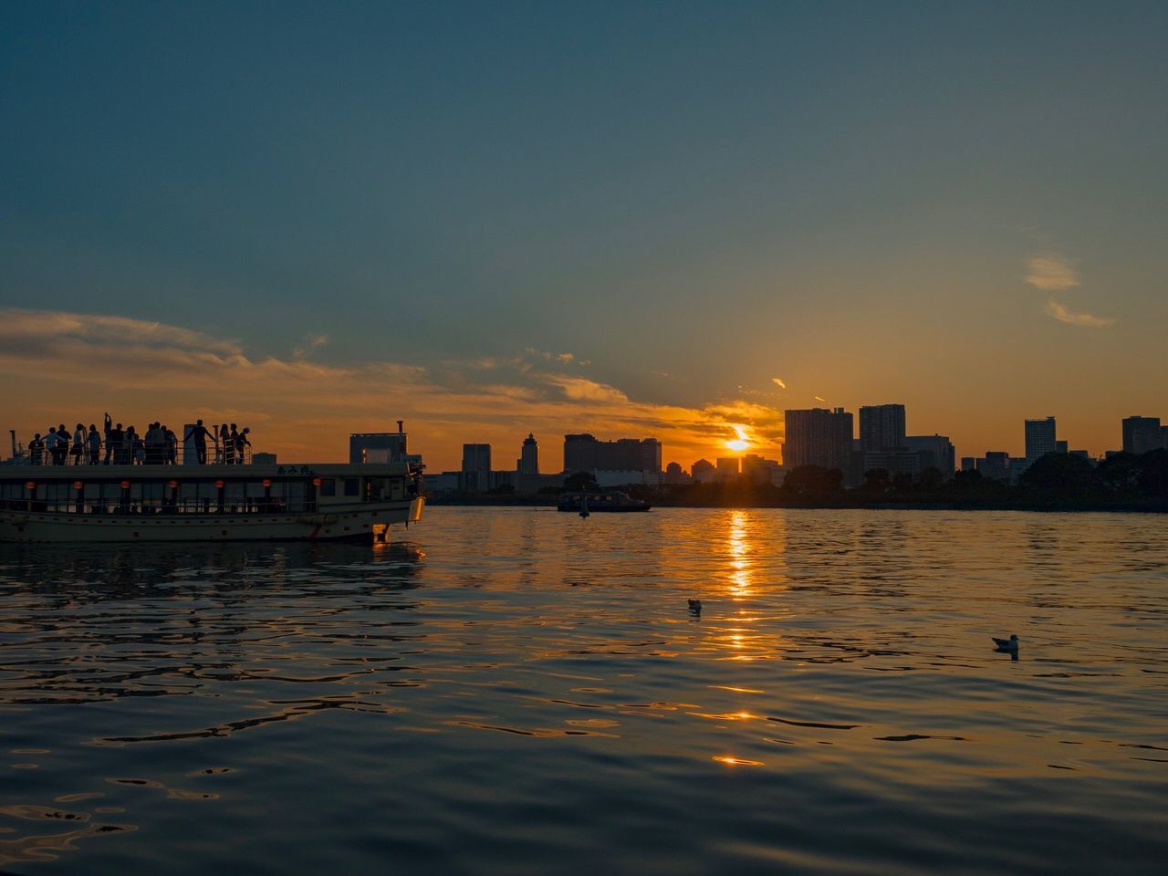 water, building exterior, architecture, city, sunset, built structure, waterfront, sky, reflection, rippled, river, cloud, scenics, sea, skyline, tranquility, tranquil scene, outdoors, nature, skyscraper, urban skyline, beauty in nature, sun, cloud - sky, moody sky, water surface