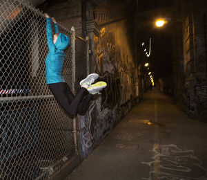 Young woman exercising on chainlink fence on illuminated bridge at night