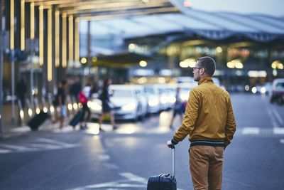 Rear view of mid adult man with luggage standing on street at airport