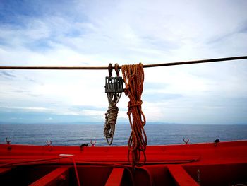 Rope hanging on railing by sea against sky