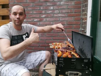 Portrait of mid adult man showing thumbs up while preparing food on barbeque grill at yard