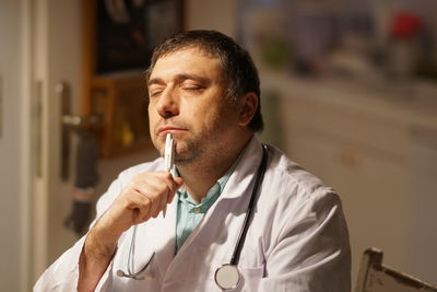 Thoughtful mature doctor with pen sitting in hospital