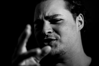 Close-up portrait of young man gesturing against black background