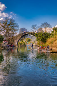 People on bridge over river against sky