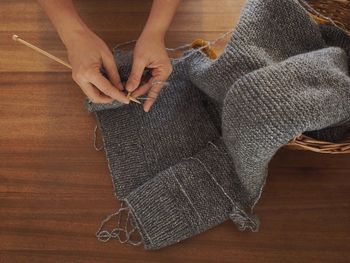 Cropped hands of woman knitting fabric at table