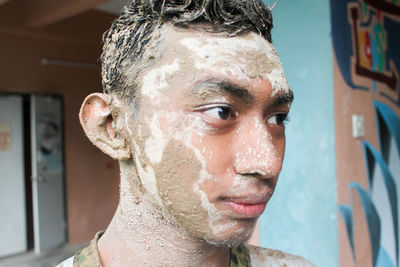 Close-up of young man with mud on face at home