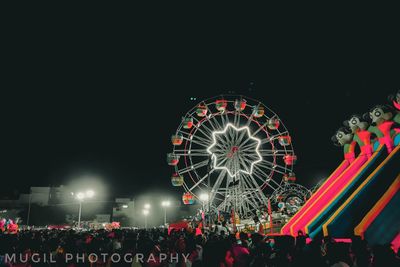 People in amusement park against sky at night