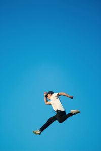 Low angle view of man jumping against clear blue sky