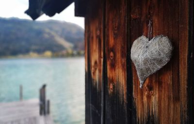 Close-up of heart shape hanging on wooden post in sea