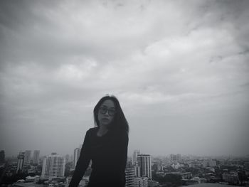 Portrait of woman standing by buildings in city against cloudy sky