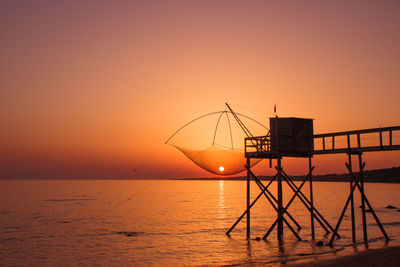 Scenic view of sea and fishing hut against orange sky