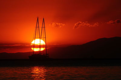 Silhouette sailboat on sea against orange sky