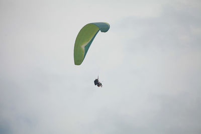 Low angle view of people paragliding against sky