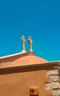 Low angle view of cross against building against clear blue sky