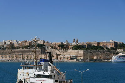 Buildings by sea against clear blue sky