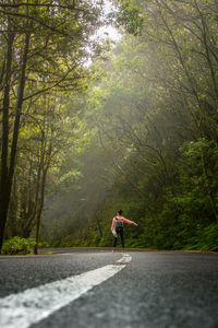 Man running on road amidst trees in forest