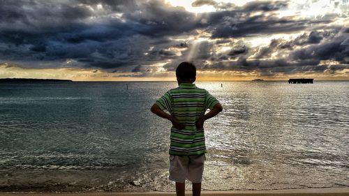 Rear view of boy standing on beach against sky