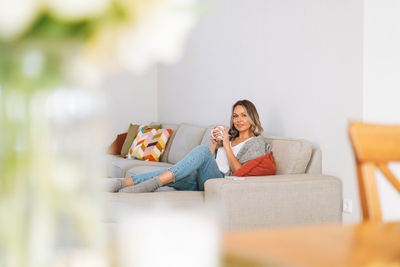 Young woman in cozy knitted grey sweater with cup of tea in hands in bright interior at home