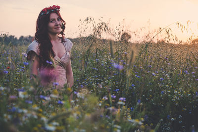 Young woman with flowers on field against sky