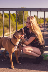 Young woman touching dog while sitting on footbridge