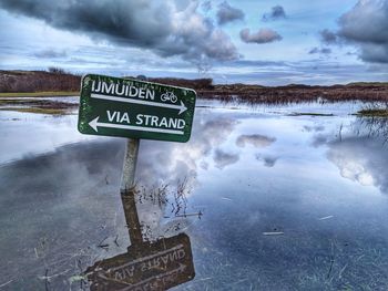 Information sign by frozen lake against sky